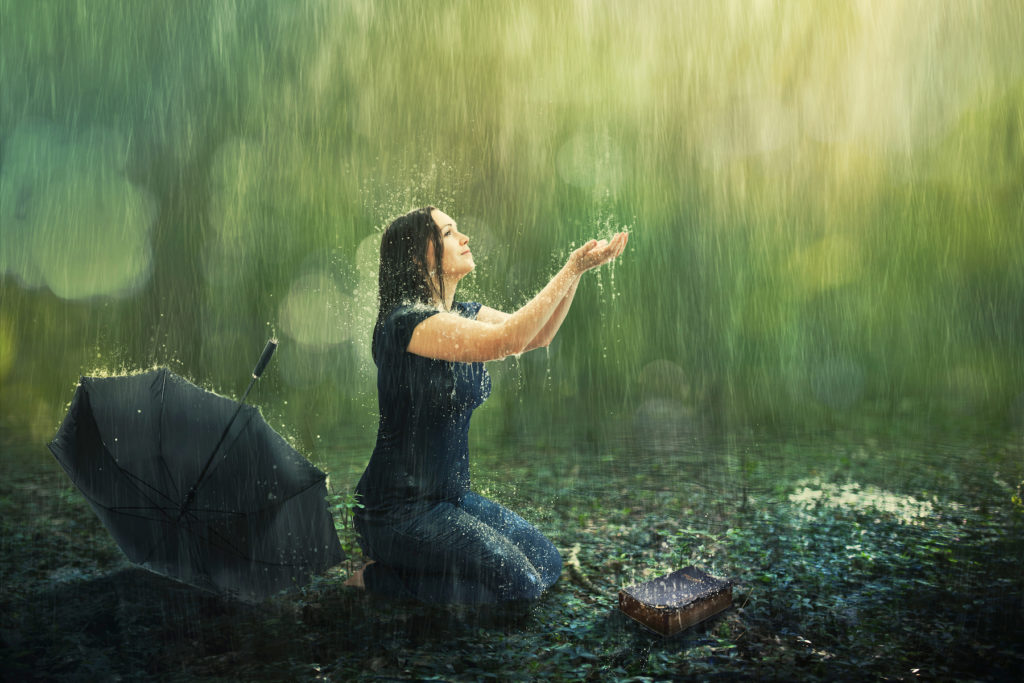 A woman enjoys a rain shower in the forest.